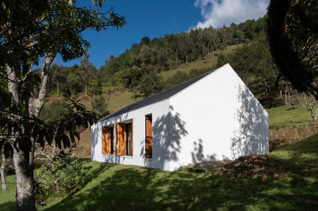 Exterior side view of Casa Florinda showcasing a smooth white plastered wall, gabled dark roof, and large wood-shuttered windows on a sloped lawn.