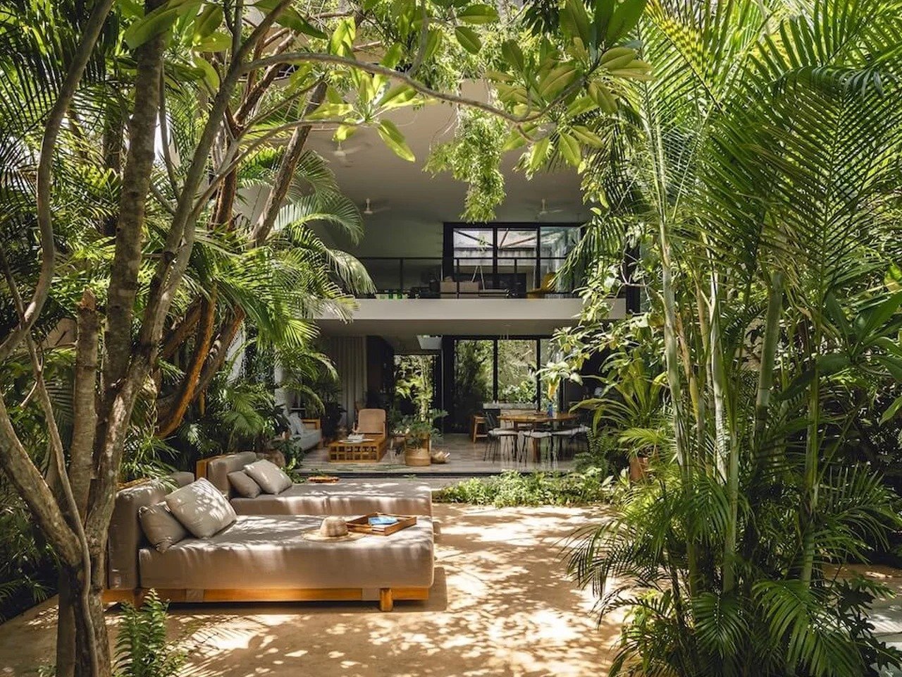 Modern two-story concrete residence nestled in lush tropical Yucatán jungle with outdoor loungers and dense green foliage at Casa del Loro by Workshop, Diseño y Construcción.