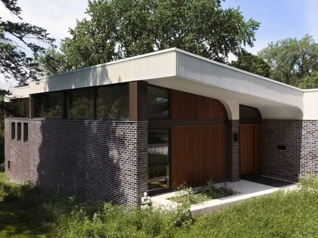 Low-profile front exterior of Crescendo home with dark brick walls, vertical wood cladding, and a curved soffit entry shelter.