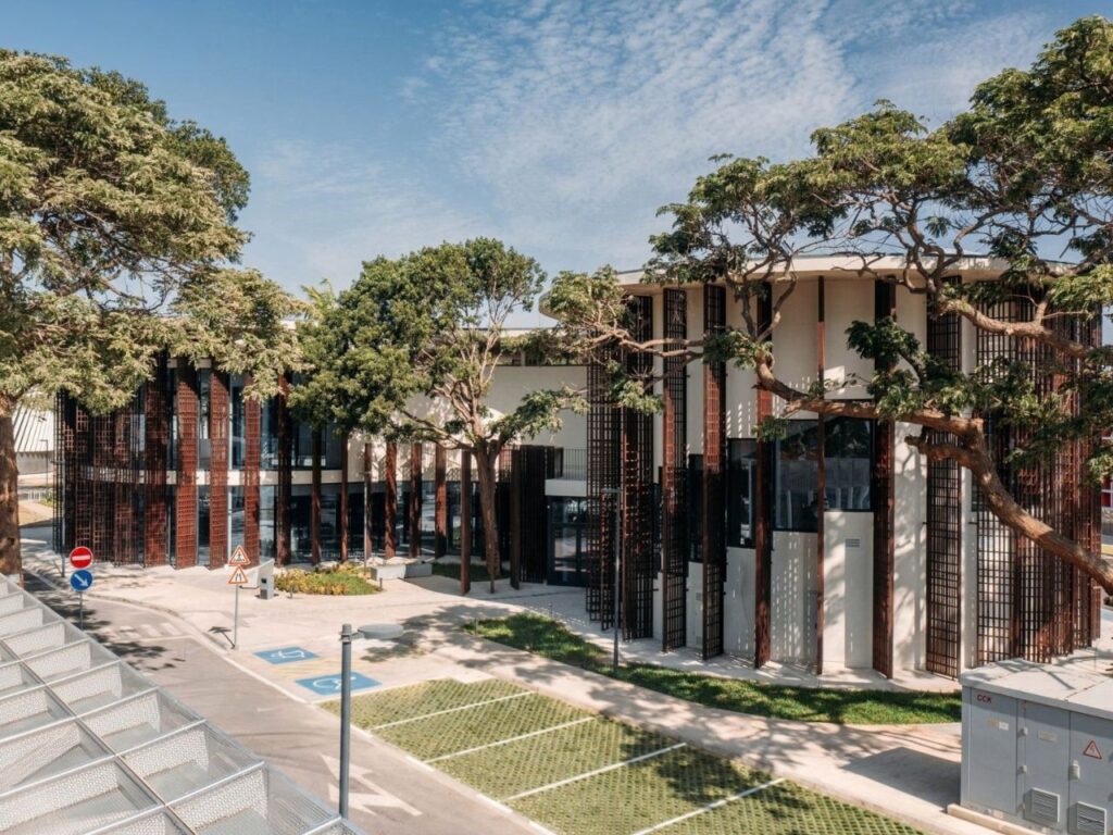 Exterior facade of Luanda Library with wooden louver screens integrated among surrounding mature trees.