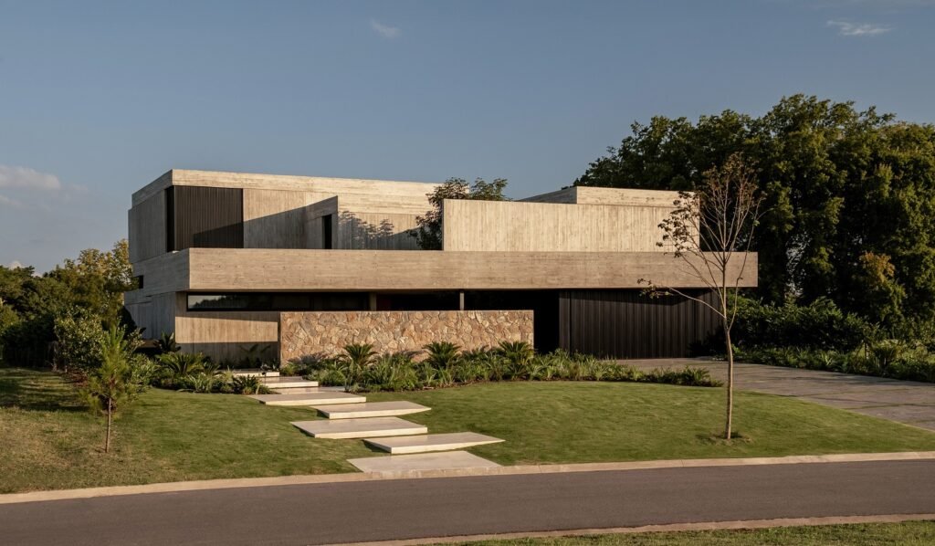Front view of Grava House exterior showing concrete facade, stone privacy wall, landscaped entry path, and driveway.