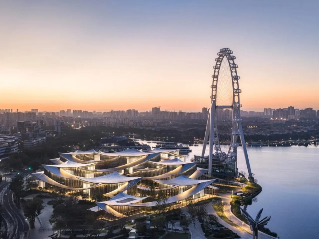 Illuminated aerial view of Suzhou Museum of Contemporary Art at dusk on the banks of Jinji Lake with city skyline.