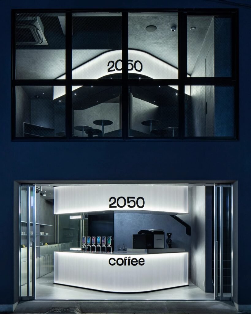 Two-story facade of 2050 Coffee featuring illuminated ground floor counter and upper floor glass window framing seating area.