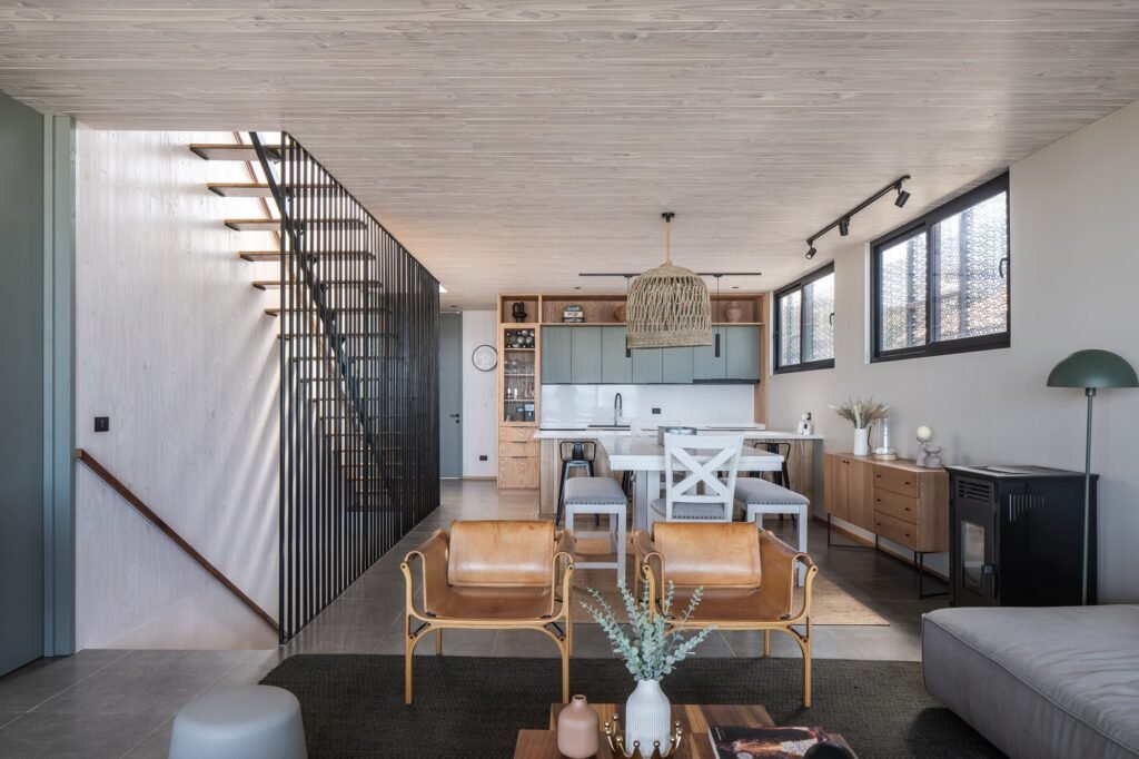 Open-plan interior living room and dining area of Gandarillas House with wooden ceiling finish, modern furniture, and a central staircase.