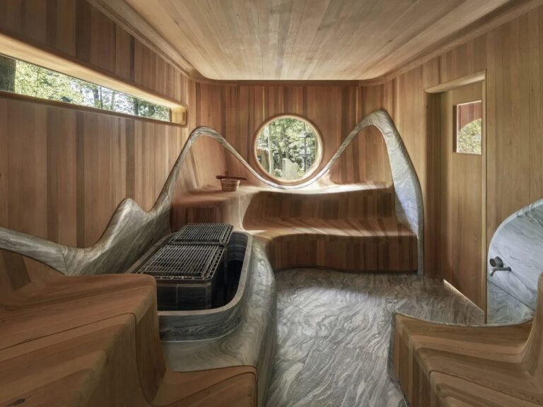 Curved cedar wood sauna interior featuring sculpted granite stove surround and round porthole window in Muskoka Island Spa.