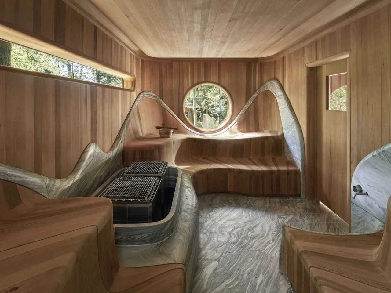 Curved cedar wood sauna interior featuring sculpted granite stove surround and round porthole window in Muskoka Island Spa.