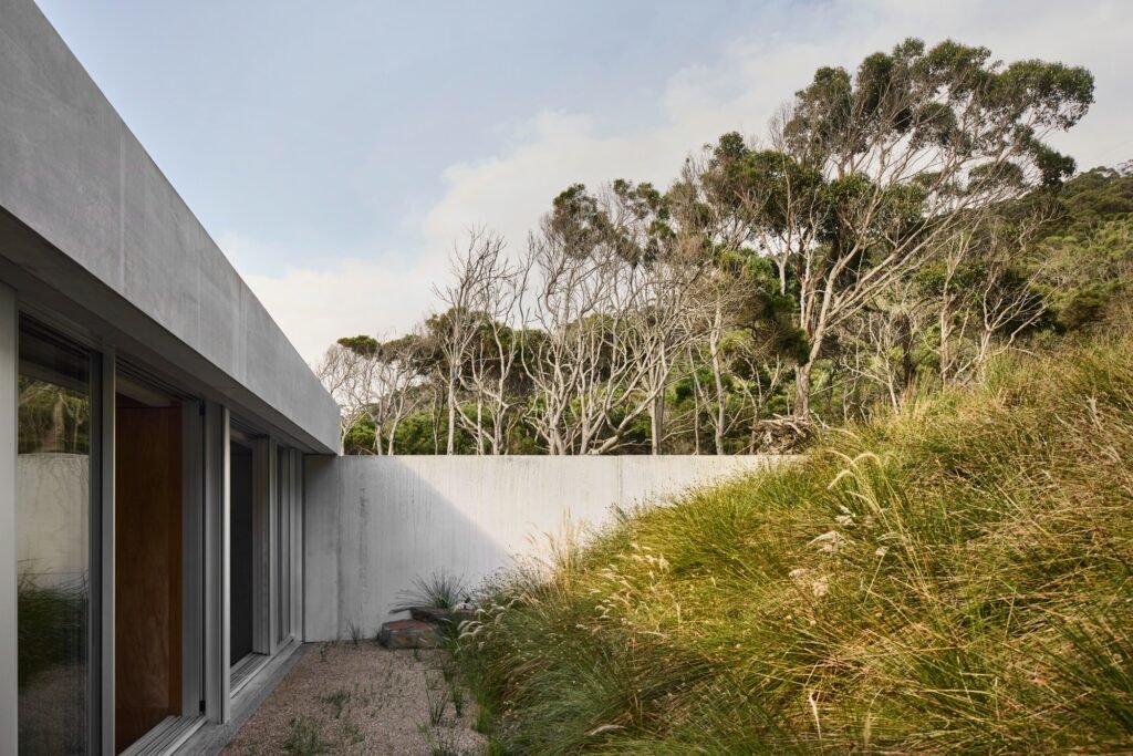 Close-up of concrete retaining wall embedded into grassy hillside leading to private bedroom entry of Otway Beach House.