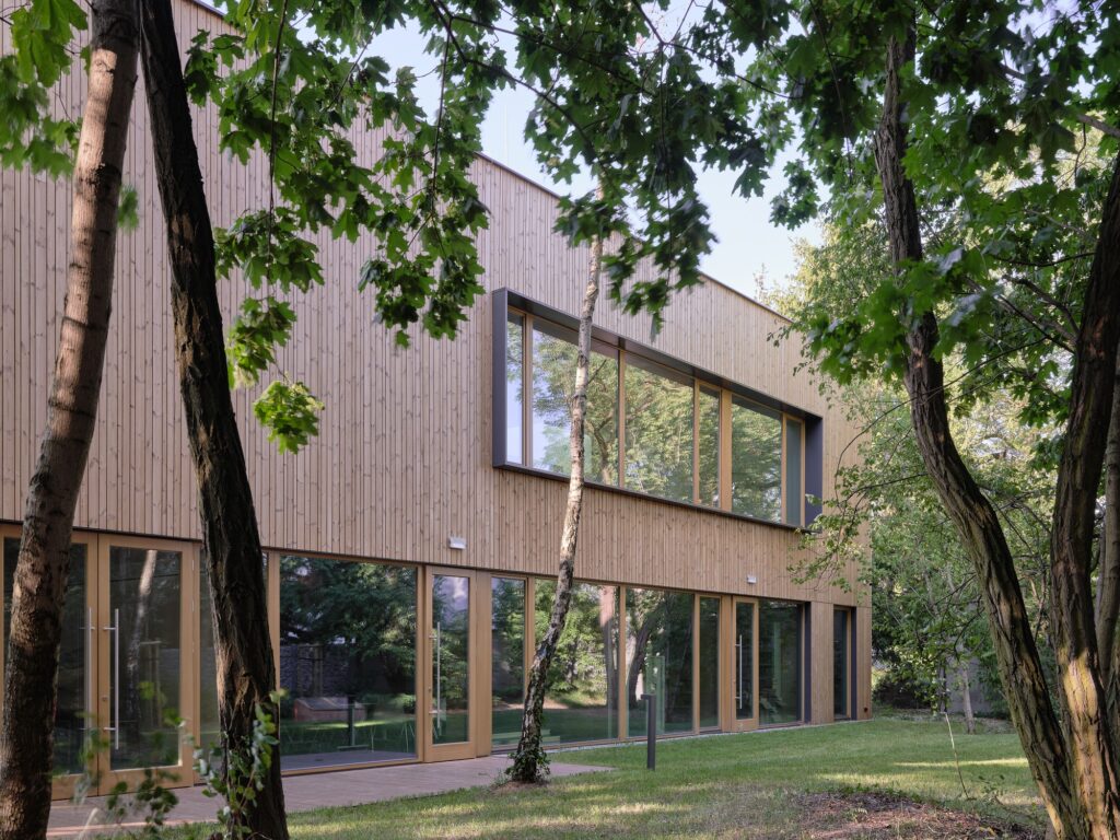 Thermally treated pine cladding and expansive glass facade of the Trzeboszka Public Library surrounded by surrounding trees.
