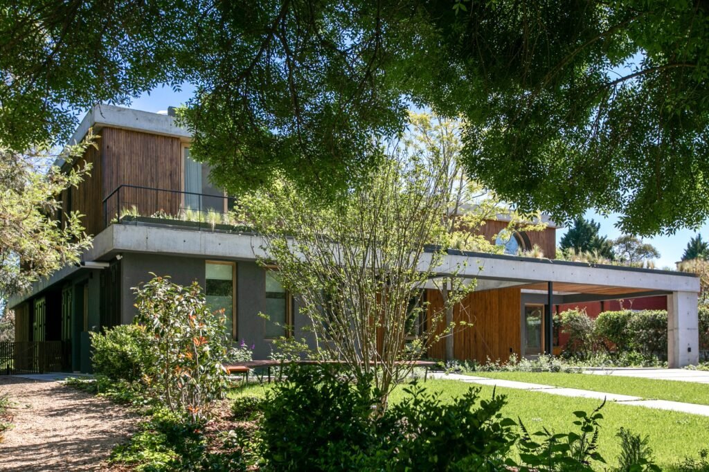Casa MDL seen from a garden path surrounded by lush trees, green lawn, and native foliage.