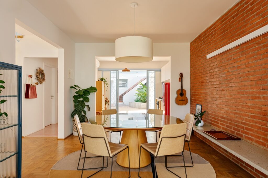 Dining area in Casa M featuring a round glass table, modern leather chairs, exposed brick wall, and original wood parquet flooring.
