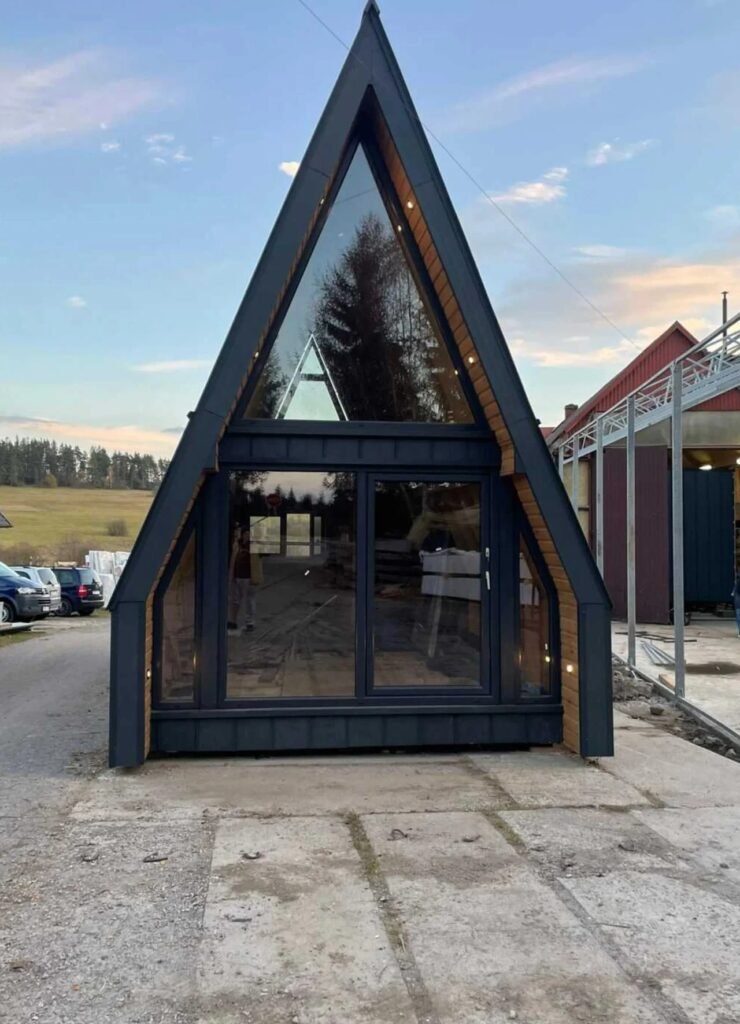 Front elevation of an A-frame cabin featuring full-height triangular glazing and sliding glass doors set in a dark aluminum frame.