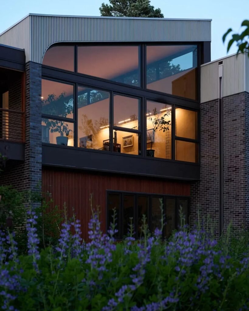 Close-up of custom trapezoidal glass windows set in black frames on the dark brick facade of Crescendo house.