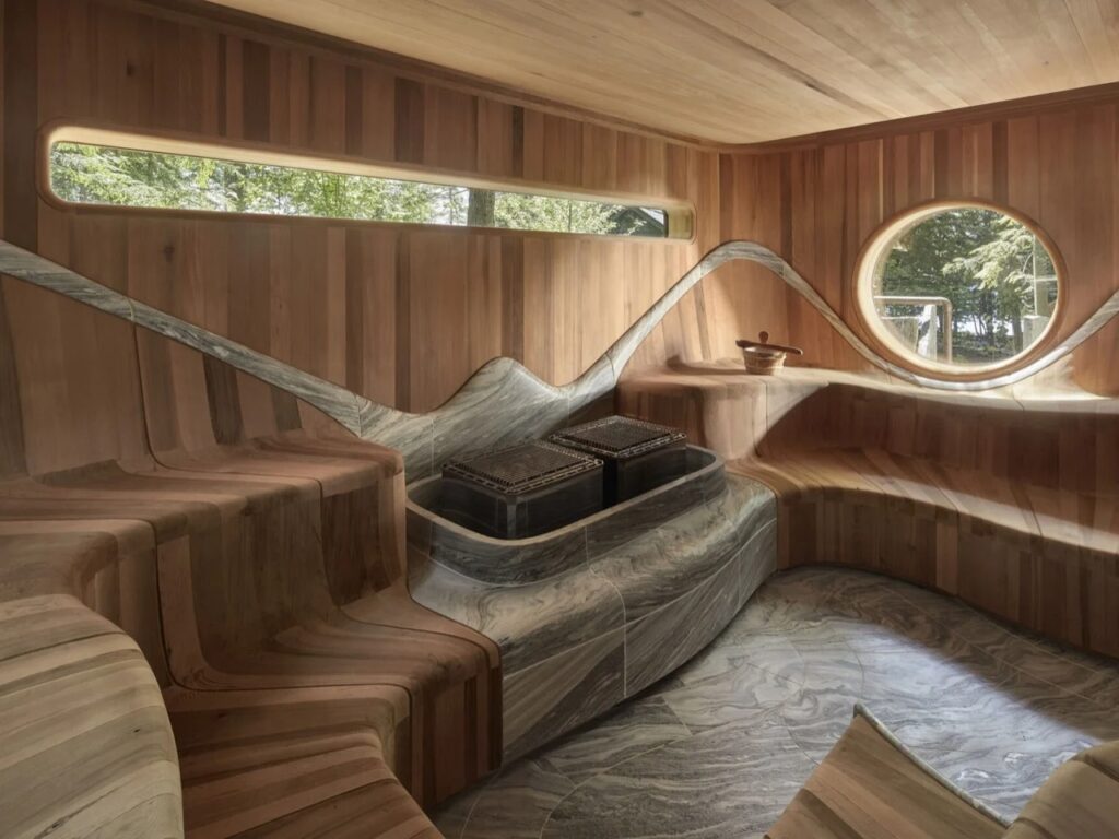 Ergonomic cedar sauna seating surrounding an integrated granite stone heater with linear horizontal window.
