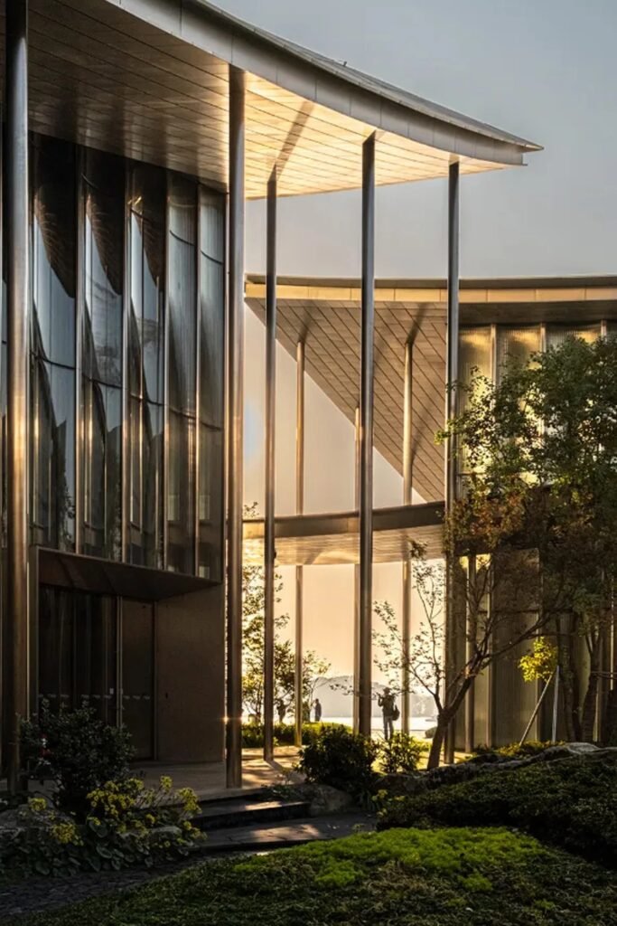 Ground-level perspective of open-air covered walkways and slender columns between museum pavilions at sunset.