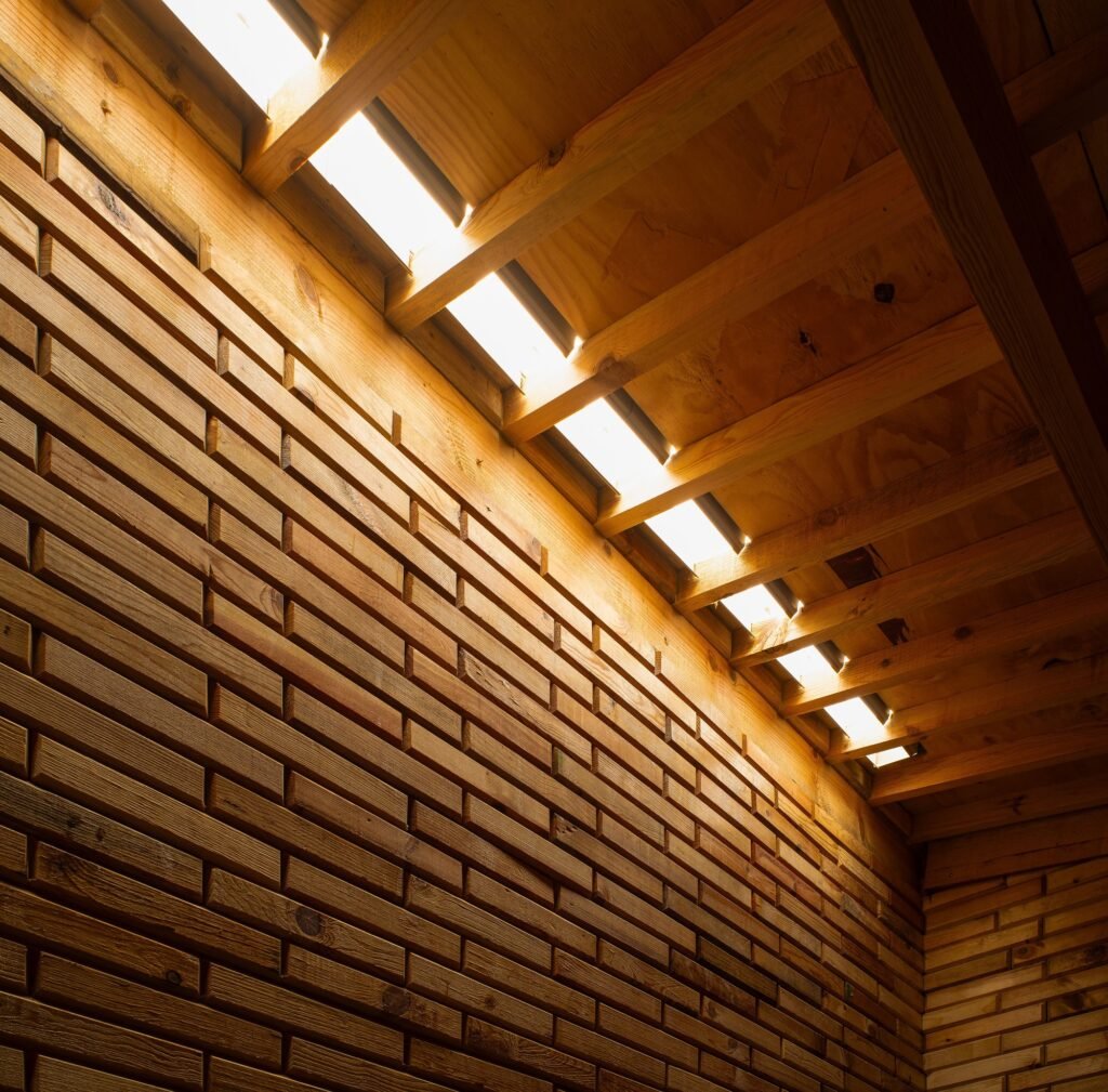 Interior view of La Grieta Pavilion showing sunlight penetrating through a narrow roof skylight gap onto wooden walls.