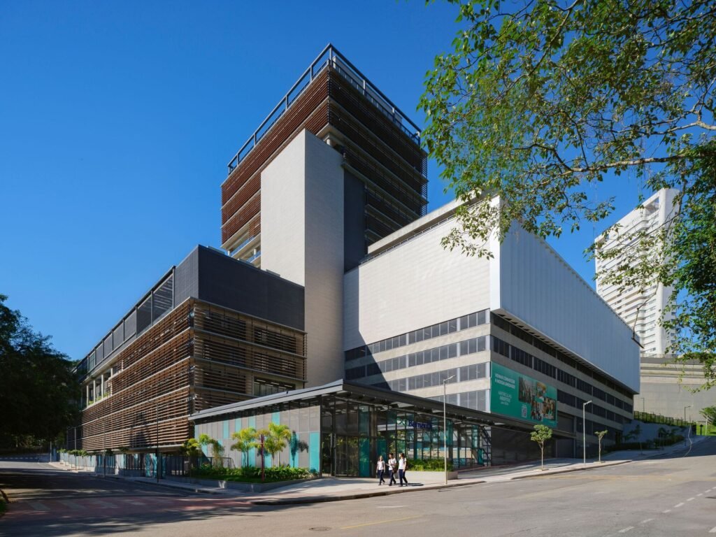 Exterior street-level perspective of Colégio Bernoulli showing the long horizontal base, glass entry, and administrative tower.