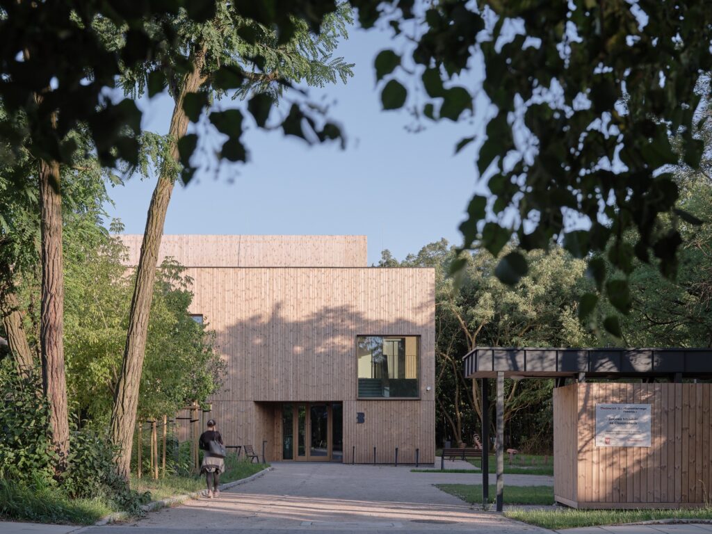 Open, fence-free entrance path leading to the modern wooden facade of the Trzeboszka Public Library.