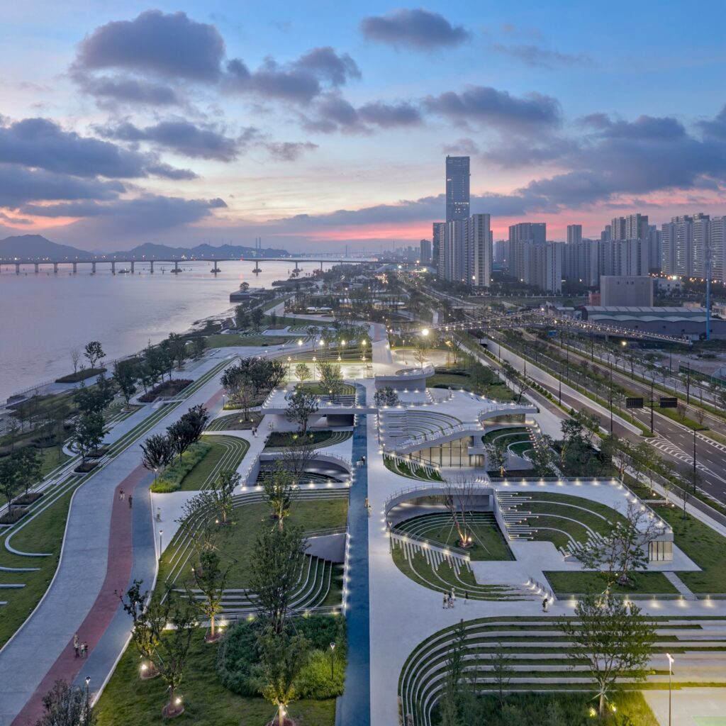 Twilight aerial view of illuminated sunken courtyards, curved architectural roof decks, and the cityscape of Taizhou bordering the river.