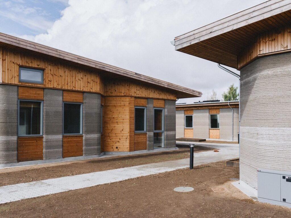 Low-rise student residential blocks featuring 3D printed concrete walls, timber cladding, and paved pedestrian paths.
