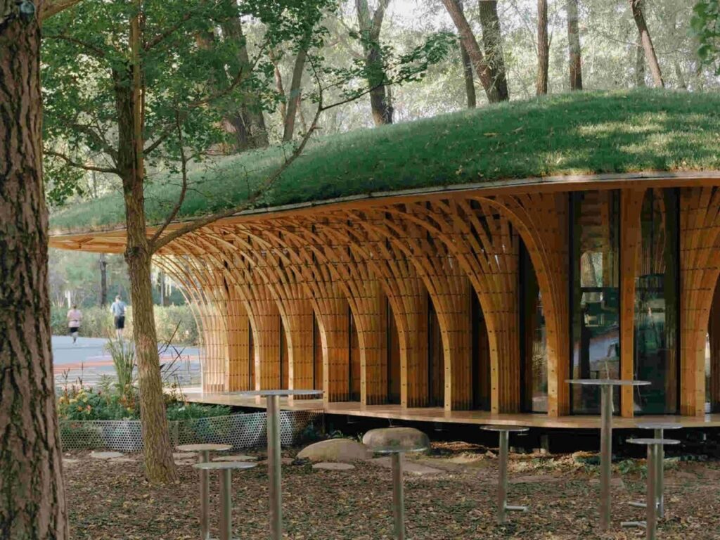 Close-up of rhythmic bent timber columns forming an open outdoor gallery deck with metallic cafe tables.