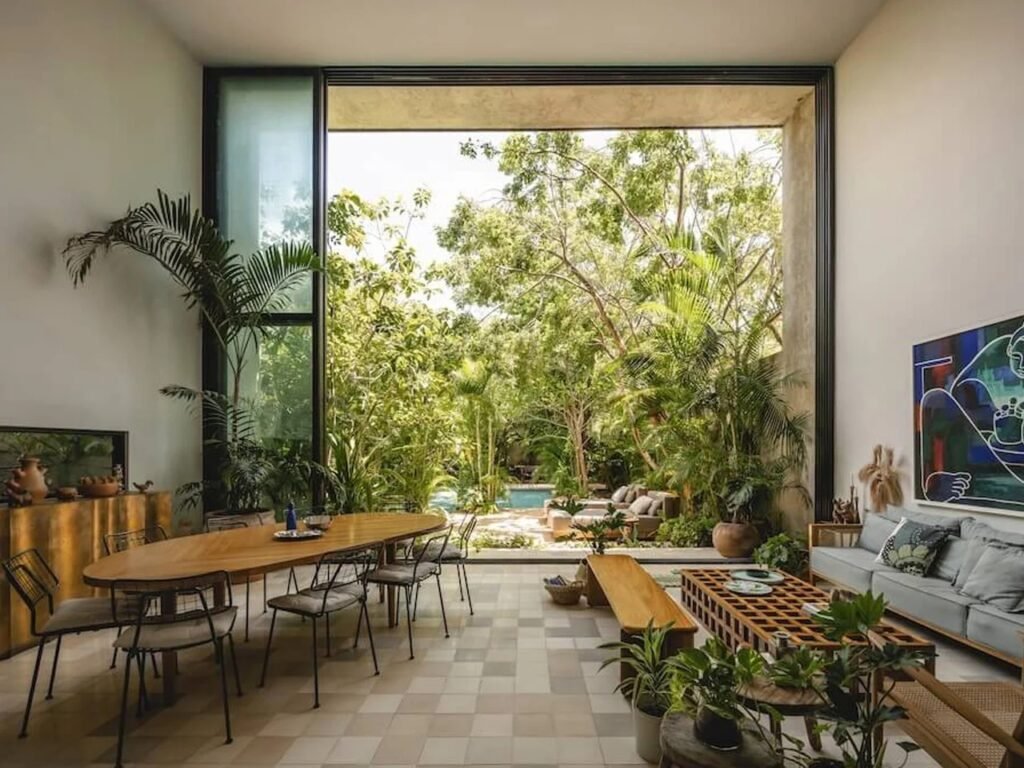 Double-height open-plan dining and living room with massive sliding glass doors opening to a lush jungle courtyard at Casa del Loro.