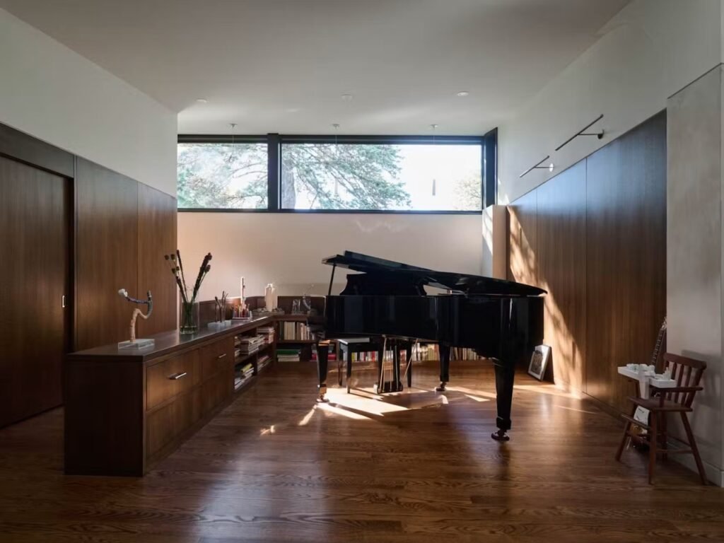 Grand piano positioned in a wood-paneled alcove illuminated by natural light from high clerestory windows in Crescendo house.