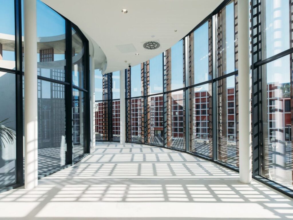 Bright interior corridor of Luanda Library with floor-to-ceiling glass walls casting grid shadow patterns.