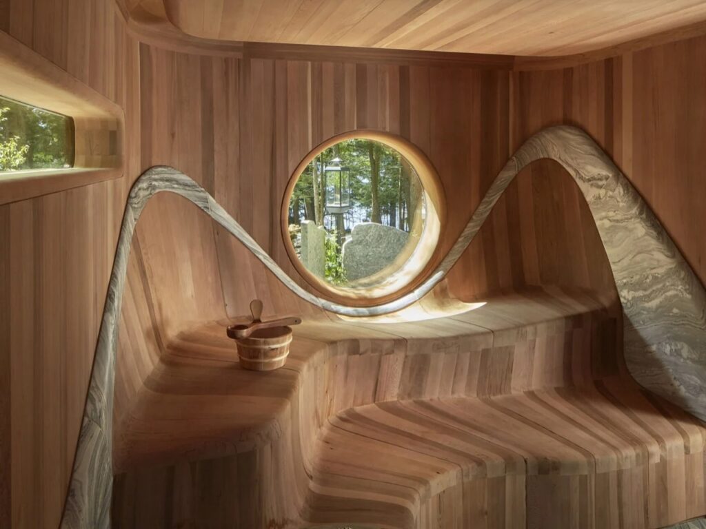 Close-up of circular window framing forest view surrounded by swooping granite trim and cedar walls in sauna.
