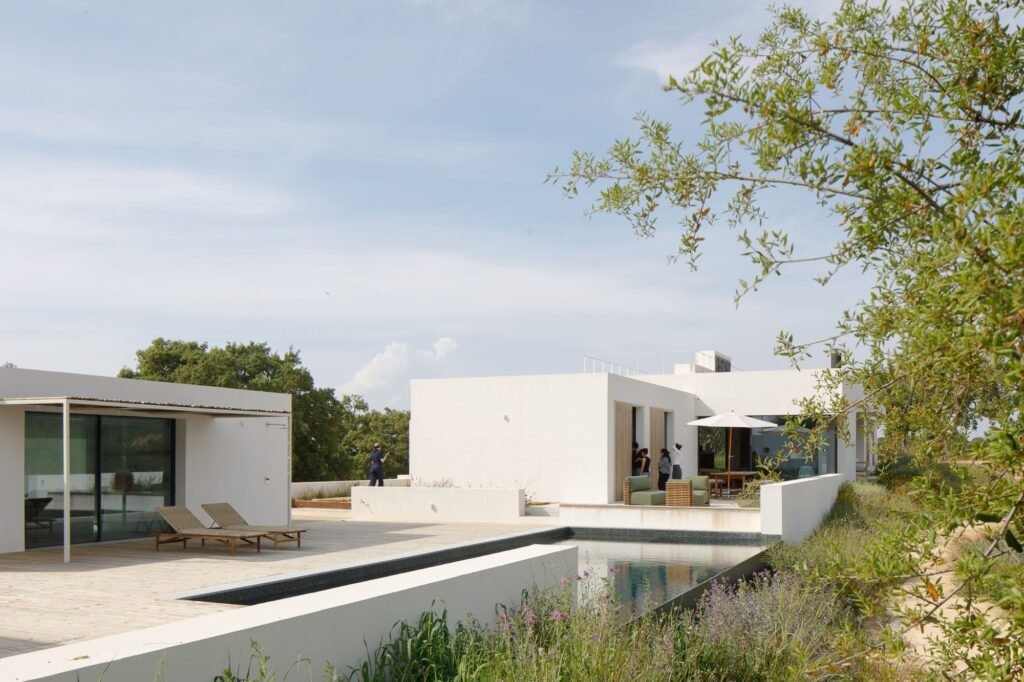 Exterior view of Melides MG House showing white detached volumes arranged around a central swimming pool and outdoor wooden deck.