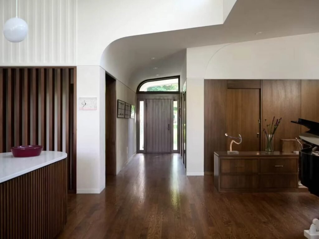 Main entrance hallway of Crescendo house with curved plaster ceiling, hardwood floors, and wood slat wall divider.
