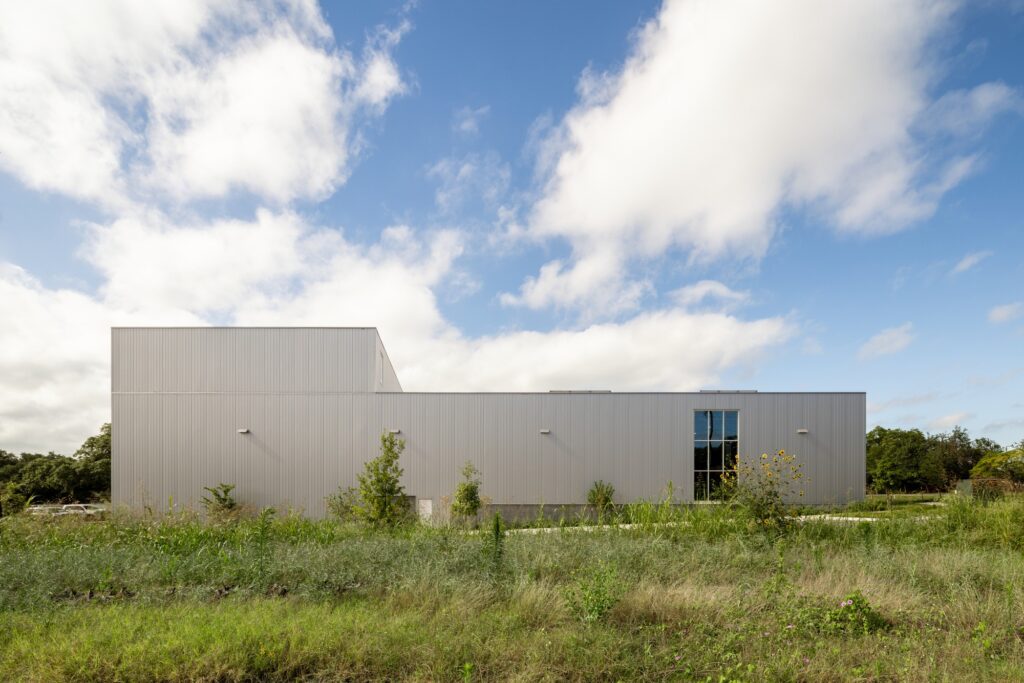 Long continuous corrugated metal north elevation of Crux South set in a green meadow under a cloudy sky.