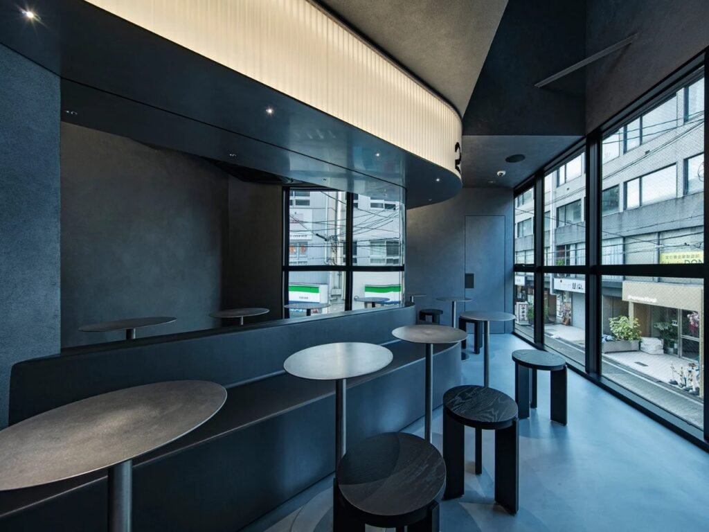 Upper floor seating area at 2050 Coffee with round tables, black stools, bench seating, and street-view glass facade.