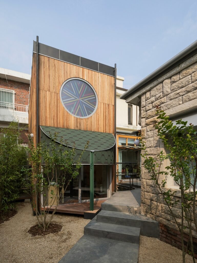 Exterior view of the wooden southern annex at Saekdong House with a circular stained-glass window, curved canopy, and stepped access path.