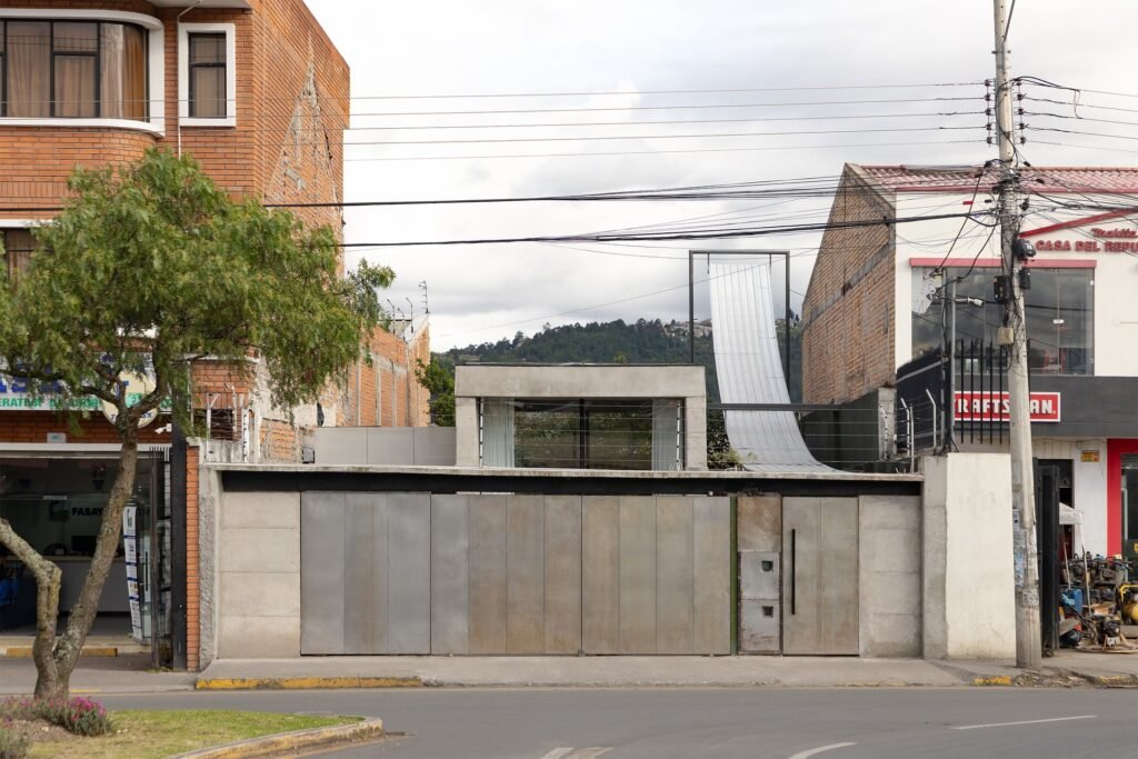 Street-level view of the residence showing concrete boundary wall, entry gate, and urban context.