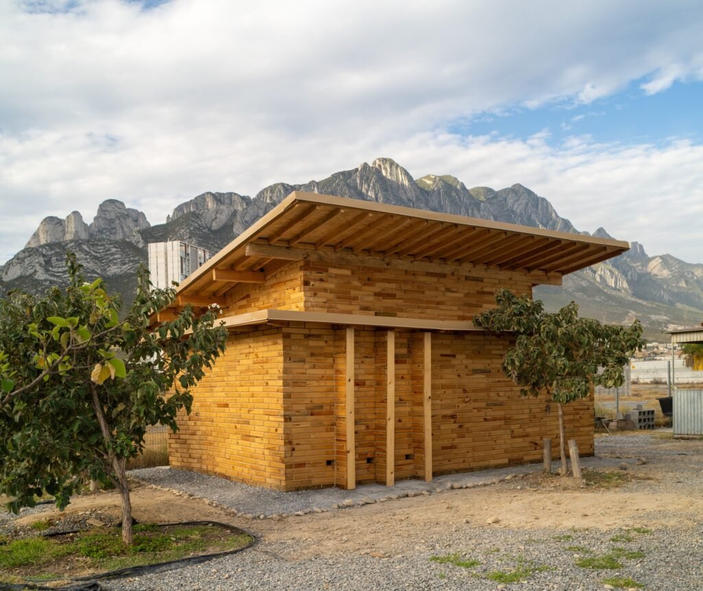 Side perspective of La Grieta Pavilion showcasing the layered wooden block walls and overhanging roof structure.