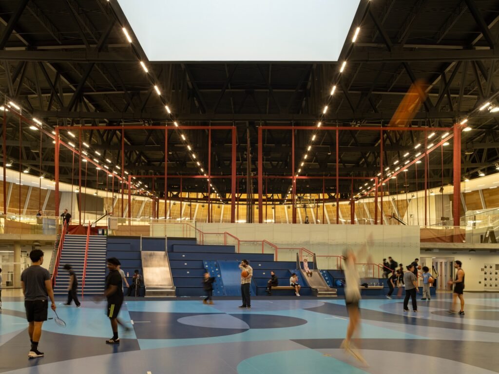 Interior view of the central urban court with people playing sports below an expansive central skylight and integrated seating steps.