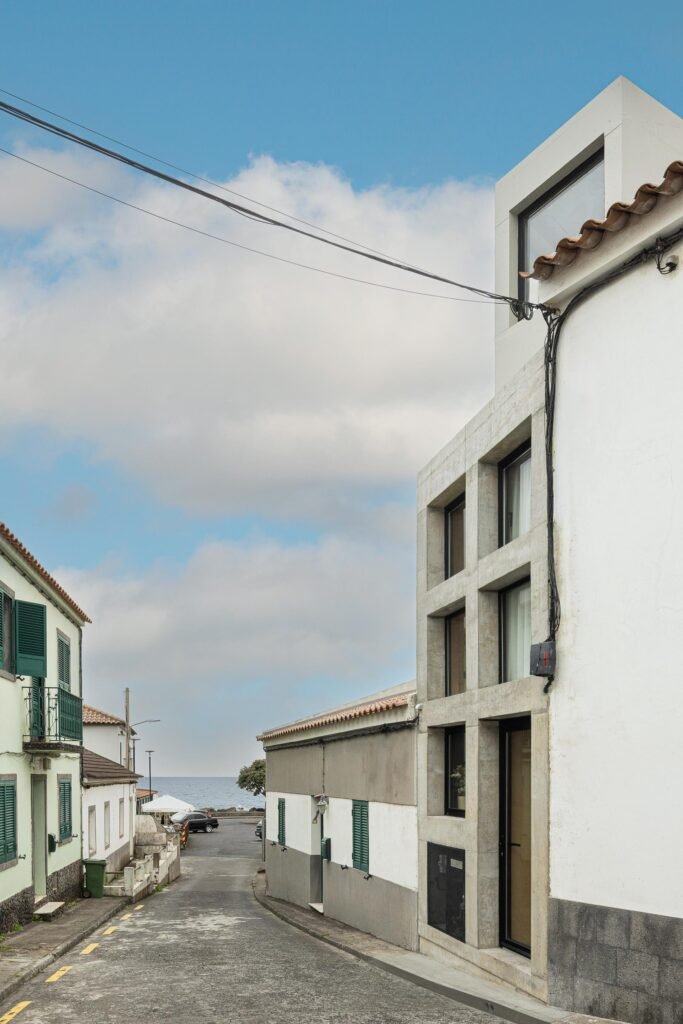 Street perspective of Mini Atalhada's exposed concrete facade leading downhill toward the ocean in S&atilde;o Miguel, Azores.