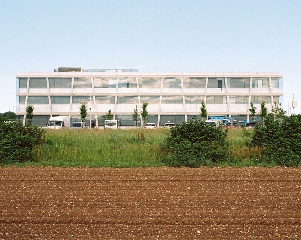 Wide horizontal elevation view of the three-story Educational Center building seen across an open agricultural field in Ljubljana.