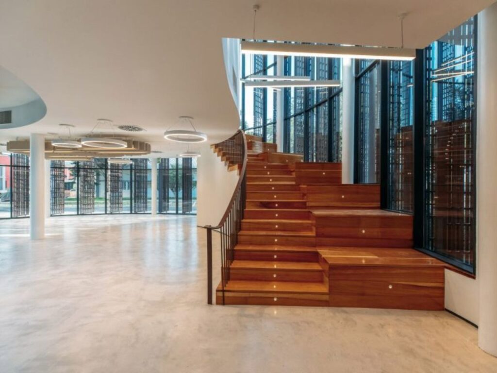 Broad wooden staircase with integrated seating steps inside the open-plan interior of Luanda Library.