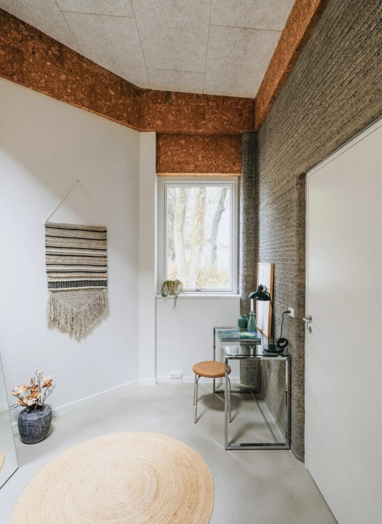 Interior study nook inside a student apartment featuring exposed 3D printed concrete walls and minimalist furniture.