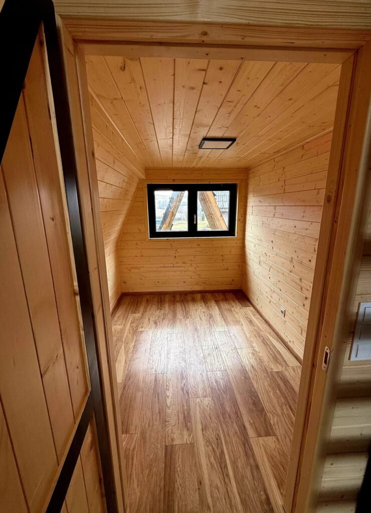 Small room with natural pine paneled walls and ceiling, hardwood flooring, and a central black-framed window.