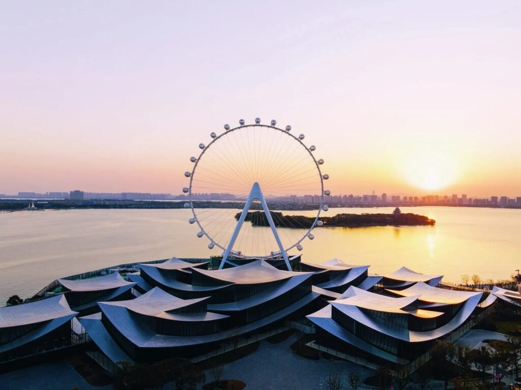 Panoramic sunset aerial view of Suzhou Museum of Contemporary Art on the edge of Jinji Lake with glowing sky.