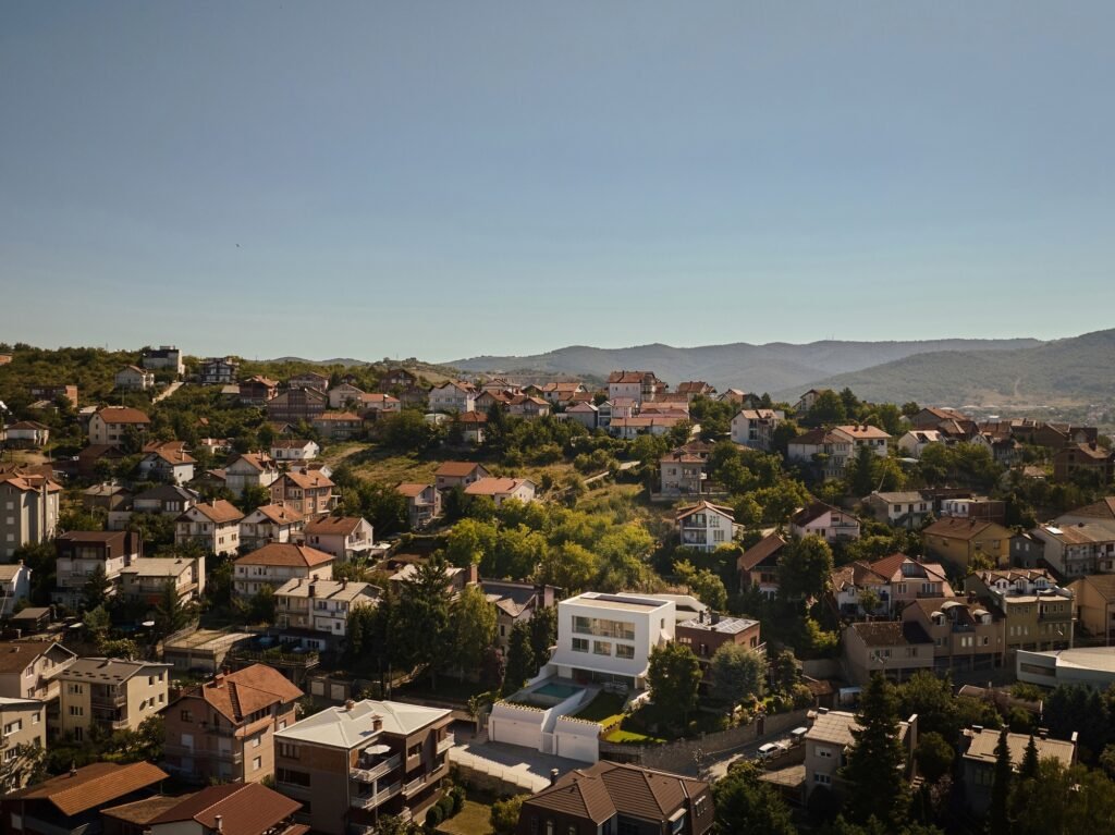 High-angle aerial view of The Gallery villa situated in a hillside residential neighborhood surrounded by greenery.