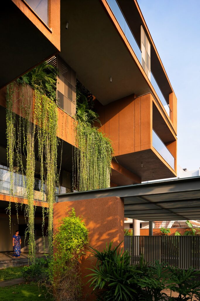 Close-up view of ground-level entrance with lush green creepers hanging down from upper level planters and a woman walking in a saree.