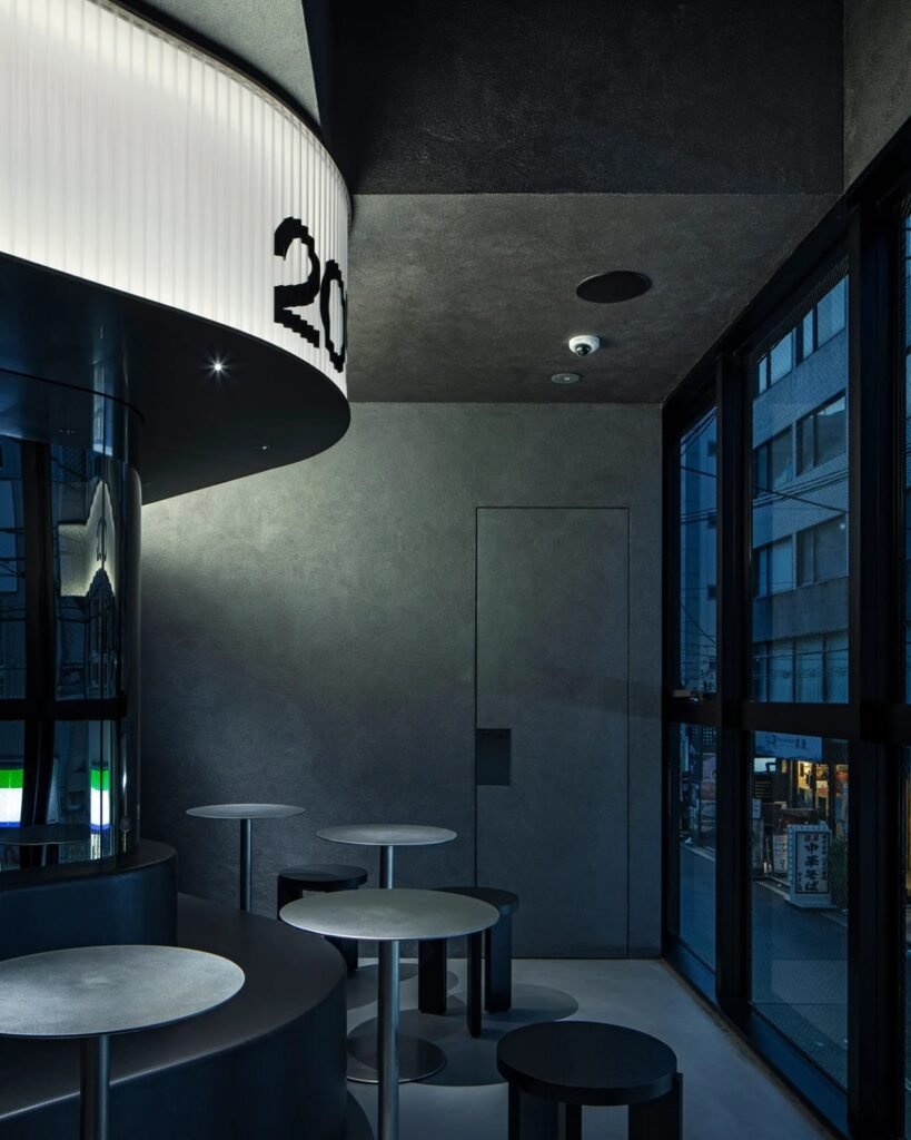 Seating area near window with custom round tables, black stools, and curved light canopy overhead.