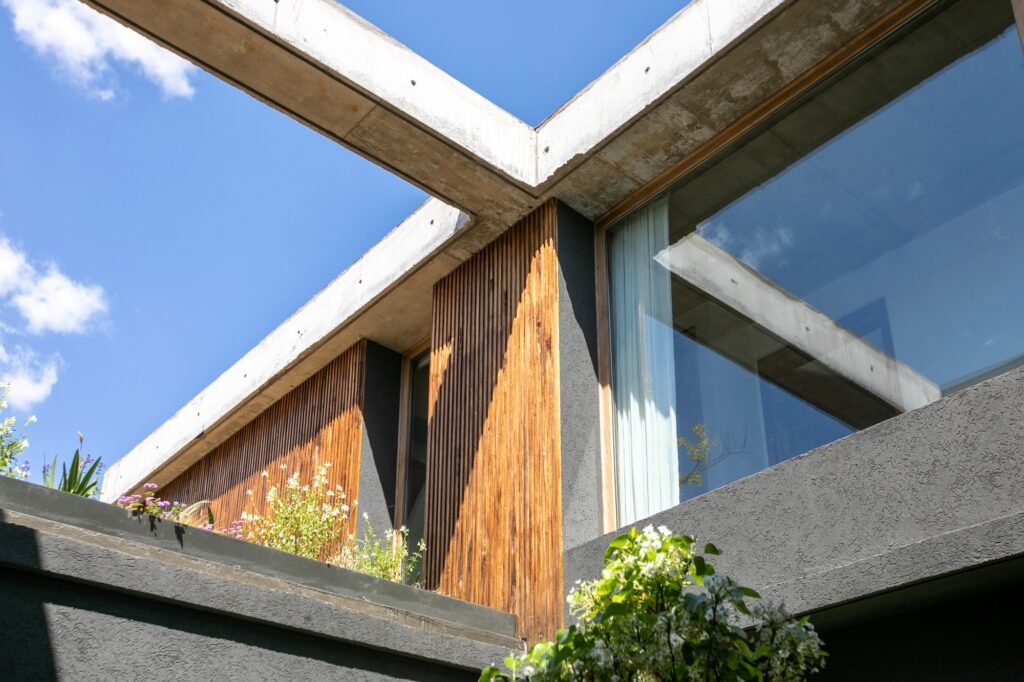 Low-angle architectural detail of Casa MDL showing concrete beams, wooden timber cladding, glass windows, and open sky.