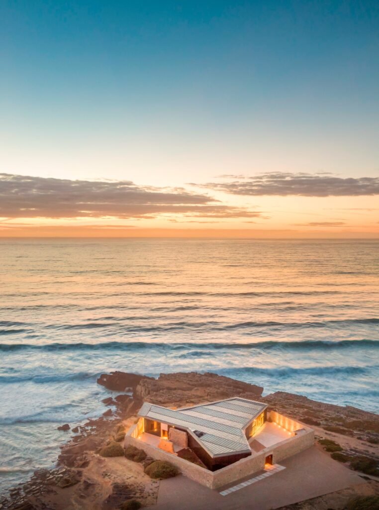 Aerial view of Cresmina Fort at dusk with warm interior lighting illuminated against the dark Atlantic ocean horizon.