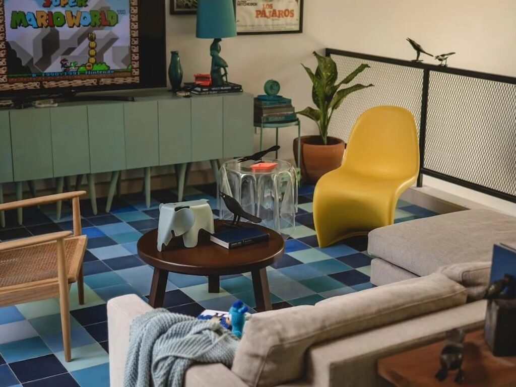 Eclectic upstairs lounge with colorful checkered floor tiles, yellow Eames-style chair, and retro decor at Casa del Loro.