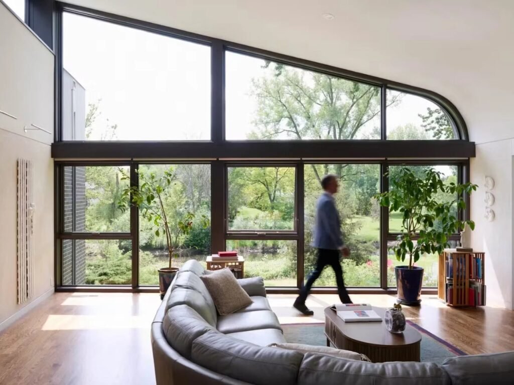 Living room in Crescendo house featuring curved leather sofa, large window wall overlooking landscape, and a person walking across the room.