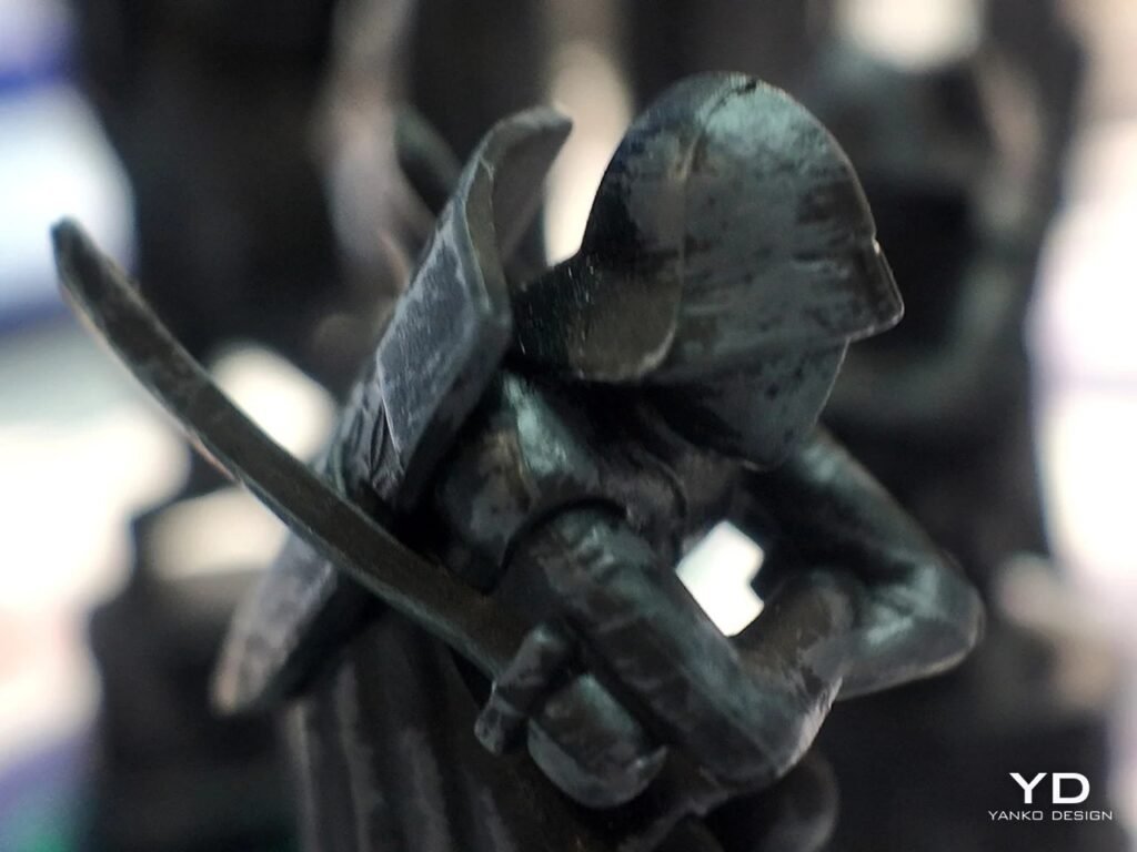 Extreme macro close-up of a dark, sculpted pawn figure holding swords with detailed stone texture.